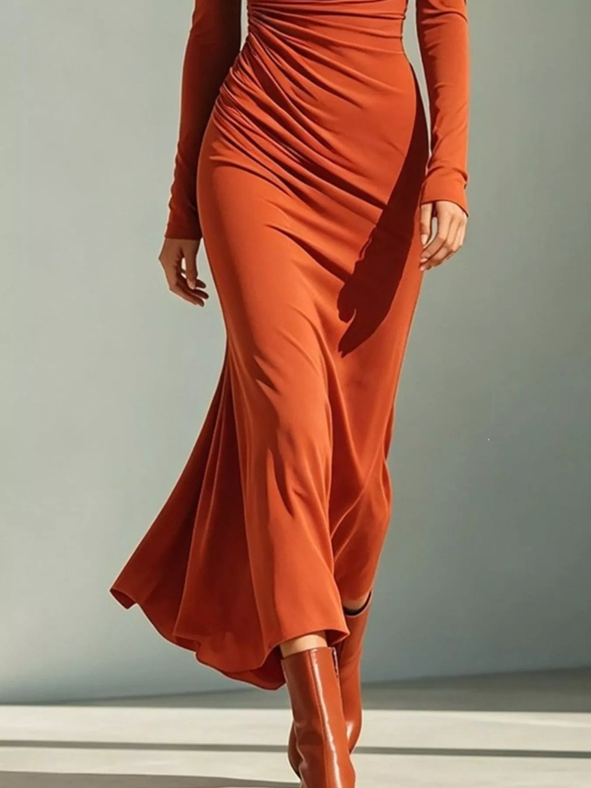Lower view of the orange ruched dress showing its flared hem and matching boots.