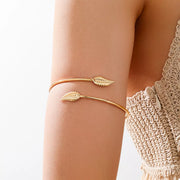 Gold-tone open cuff bracelet with two leaf accents worn on wrist