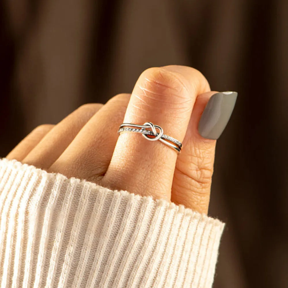 Silver knot ring worn on a hand against a dark background