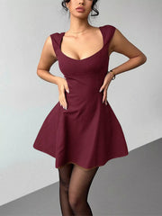 Model poses in the burgundy sleeveless mini dress with hands at waist