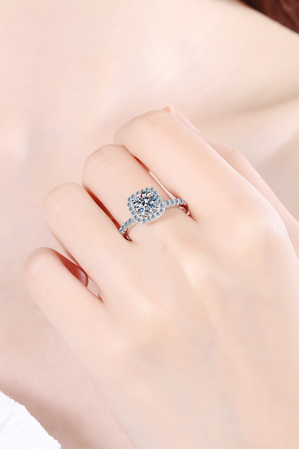 Close-up of square halo moissanite ring worn on a model’s finger.