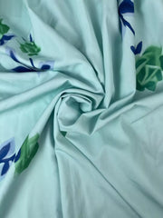 Close-up of aqua fabric with blue floral embroidery and gathered folds.