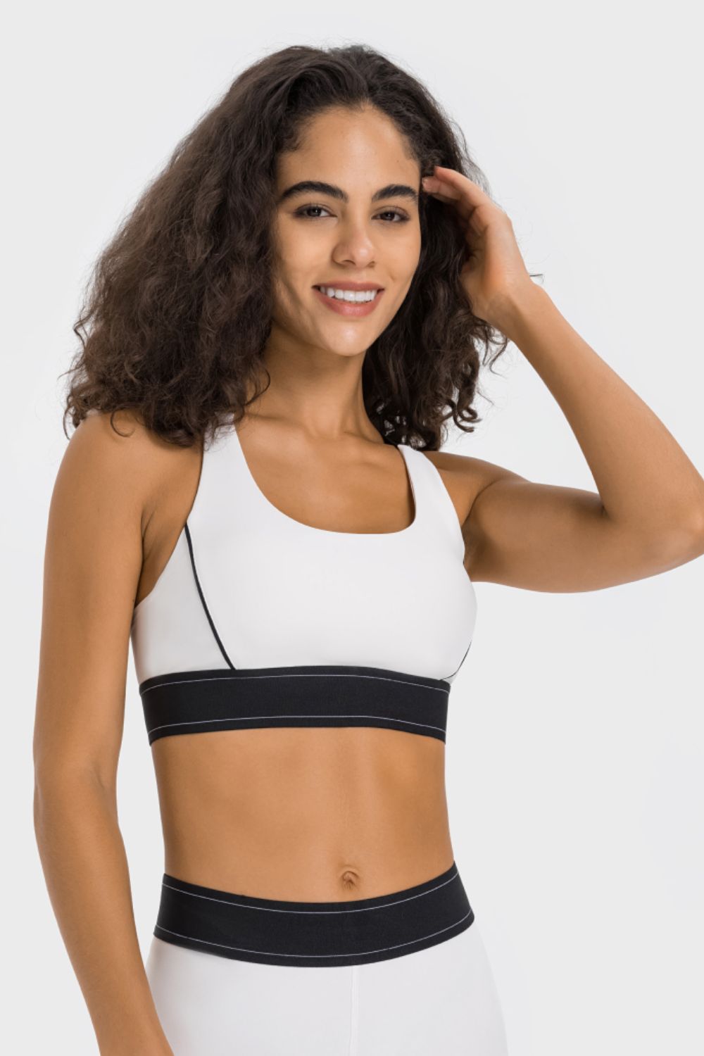 Model wearing a white sports bra with black contrast piping and hem