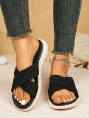 Front view of black cross-strap slide sandals with white soles worn with cropped jeans