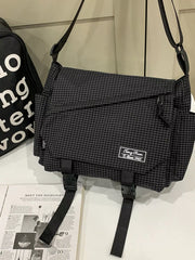 Black checked messenger bag with front zip pocket, side pockets and hanging buckle straps, displayed against white