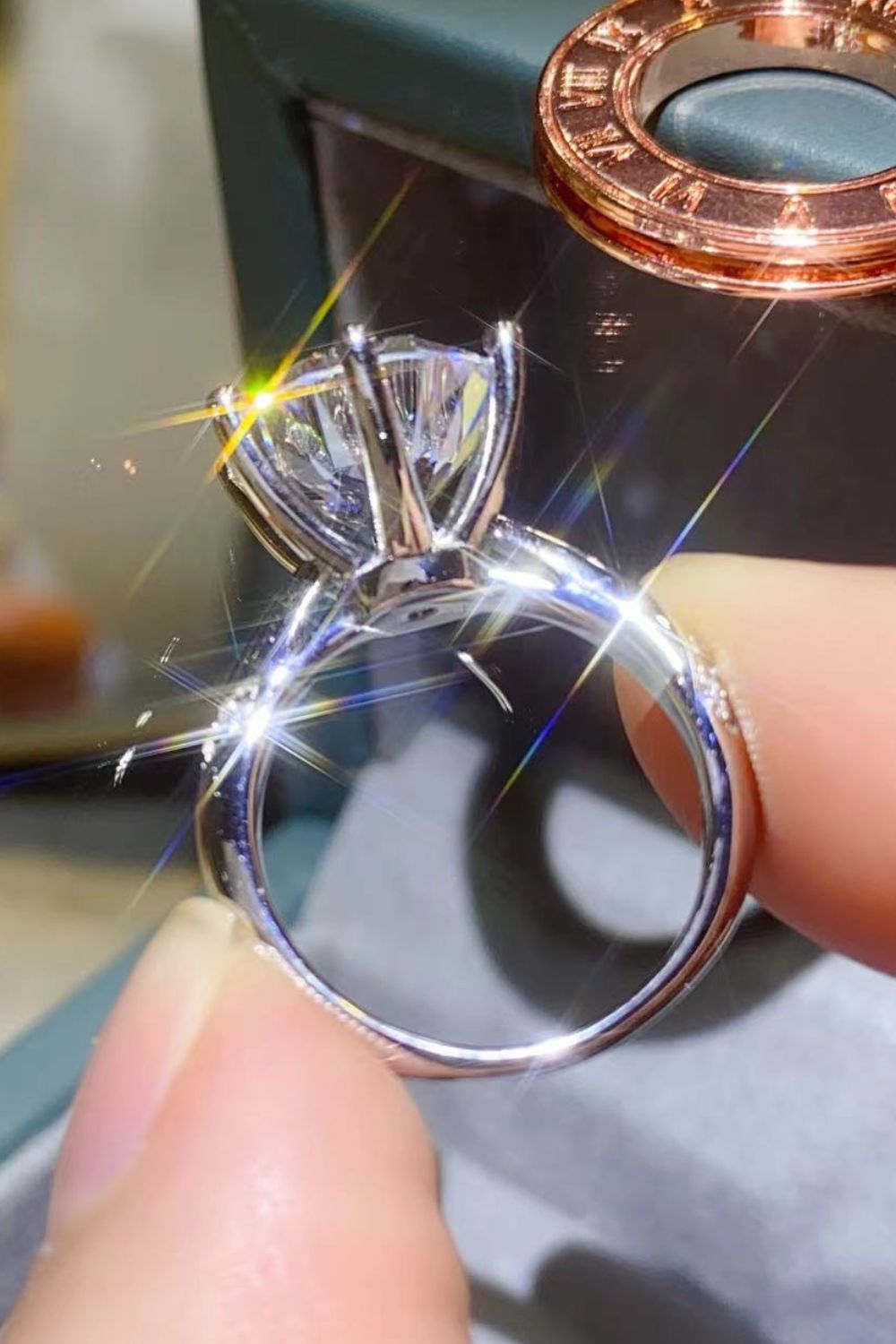 Profile view of the six-prong solitaire ring held between fingers against a dark display.