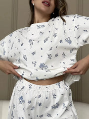 Model wearing white lounge top with dark botanical sprigs and matching elastic-waist shorts