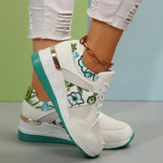 White sneakers with green floral panels and turquoise wedge soles worn on feet