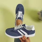 Navy flat shoe with white stripes held in hand, side view