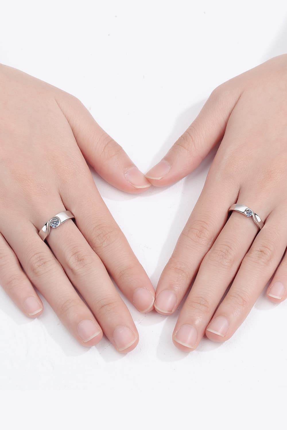 Pair of moissanite rings modeled on hands, showing their slim silver bands.