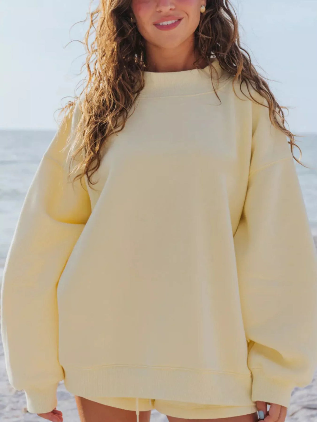 Front view of a pale yellow oversized sweatshirt and matching shorts at the beach.
