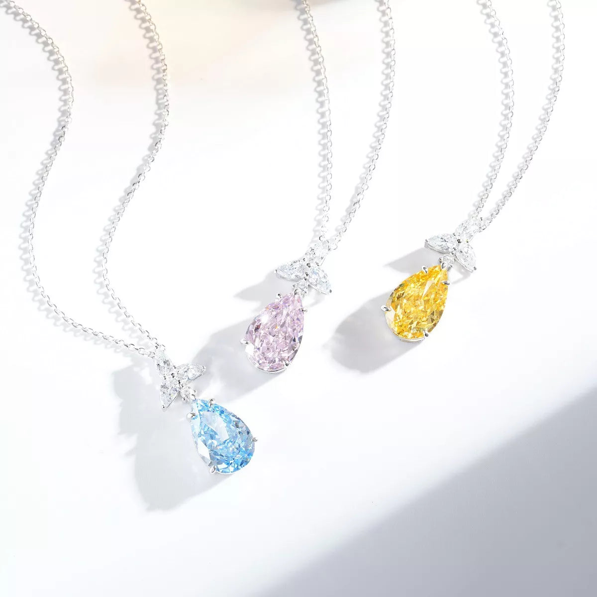 Three teardrop zircon necklaces in pastel blue, blush pink and light yellow on a white display