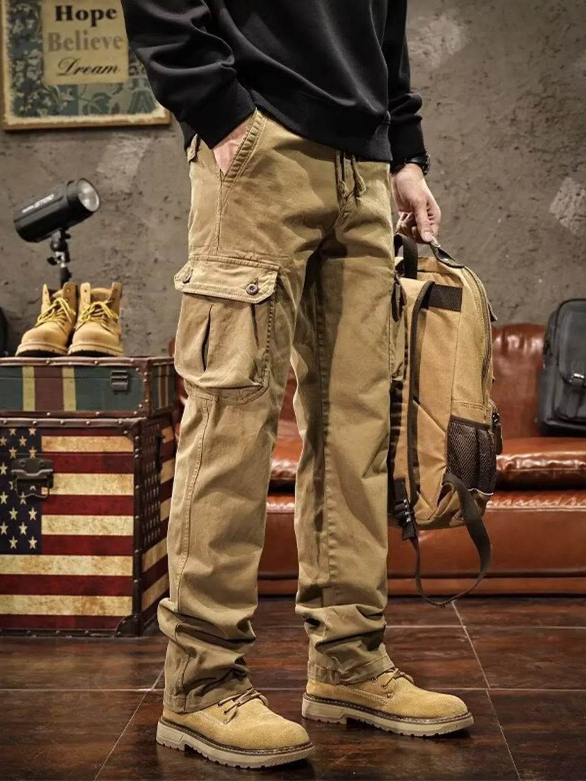 Tan cargo pants with multiple flap pockets modeled with a black sweatshirt.