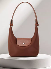 Brown shoulder bag displayed upright with short handle and textured front flap on a pedestal.
