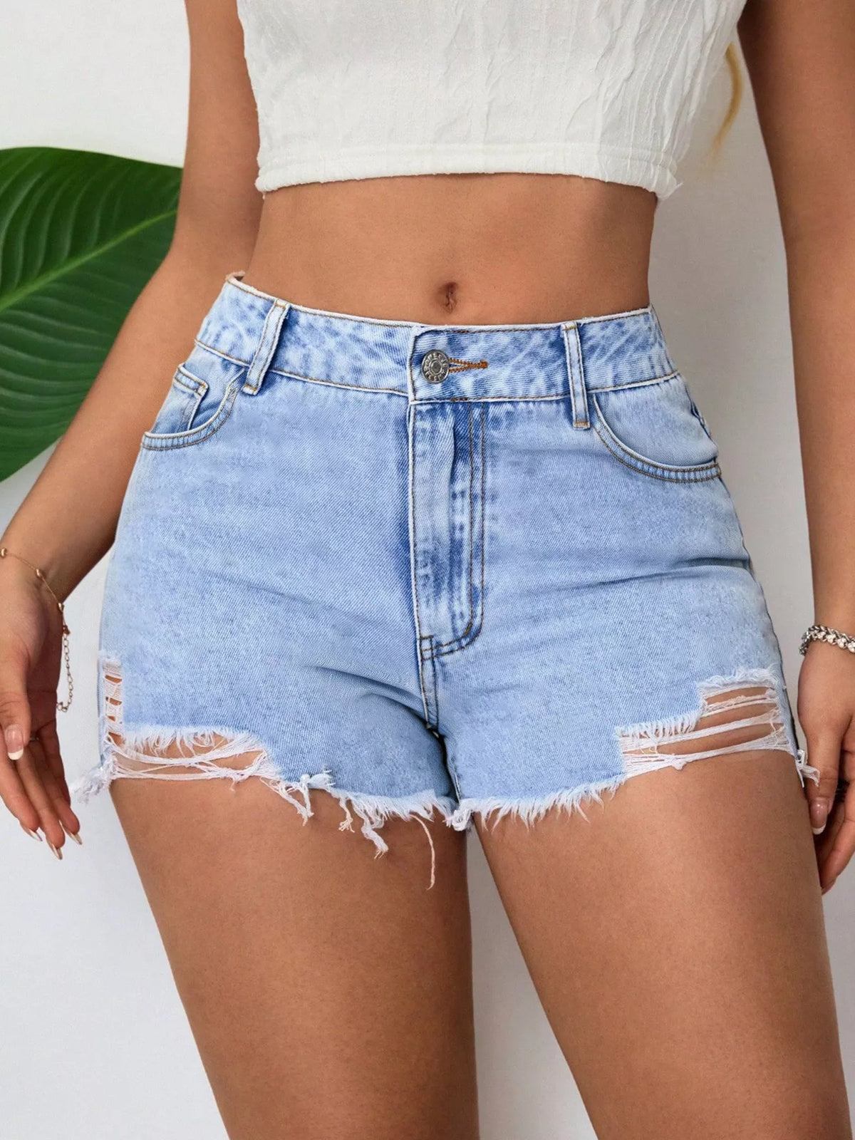 Front view of distressed light-wash denim shorts with ripped details and raw hems