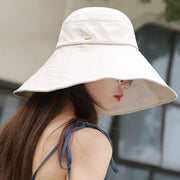 Model wearing a beige wide-brim sun hat with stitched brim and a small side emblem.