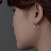 Side view of silver heart-shaped dangle earring worn on an ear