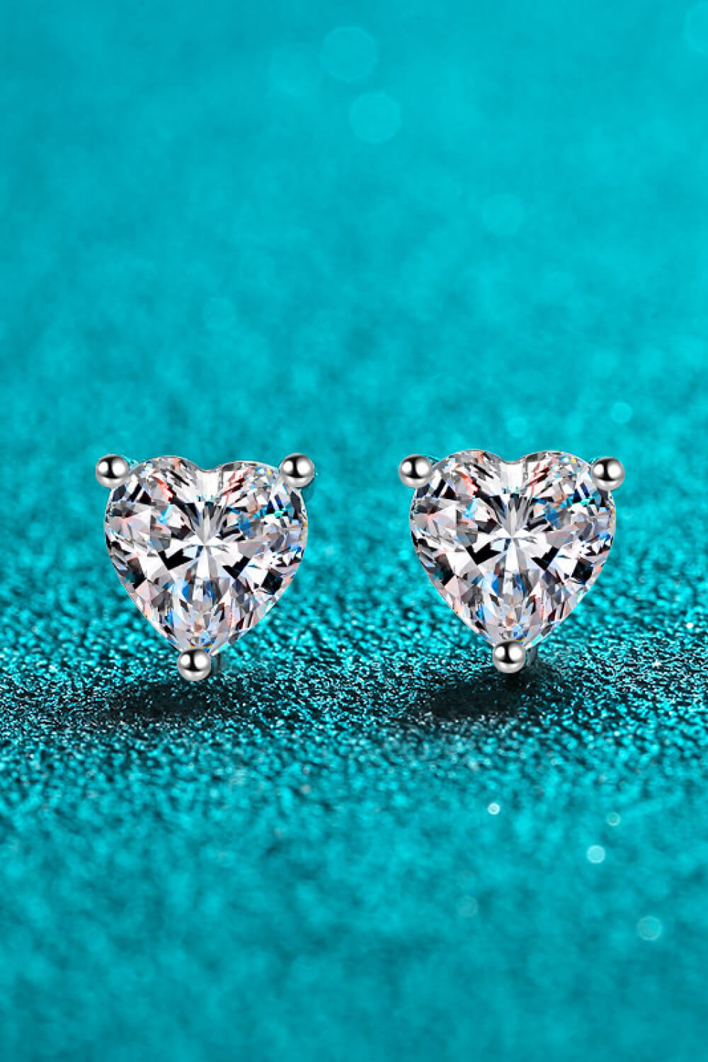 2 Carat Moissanite Heart-Shaped Stud Earrings — Front view of heart-shaped moissanite earrings on teal background