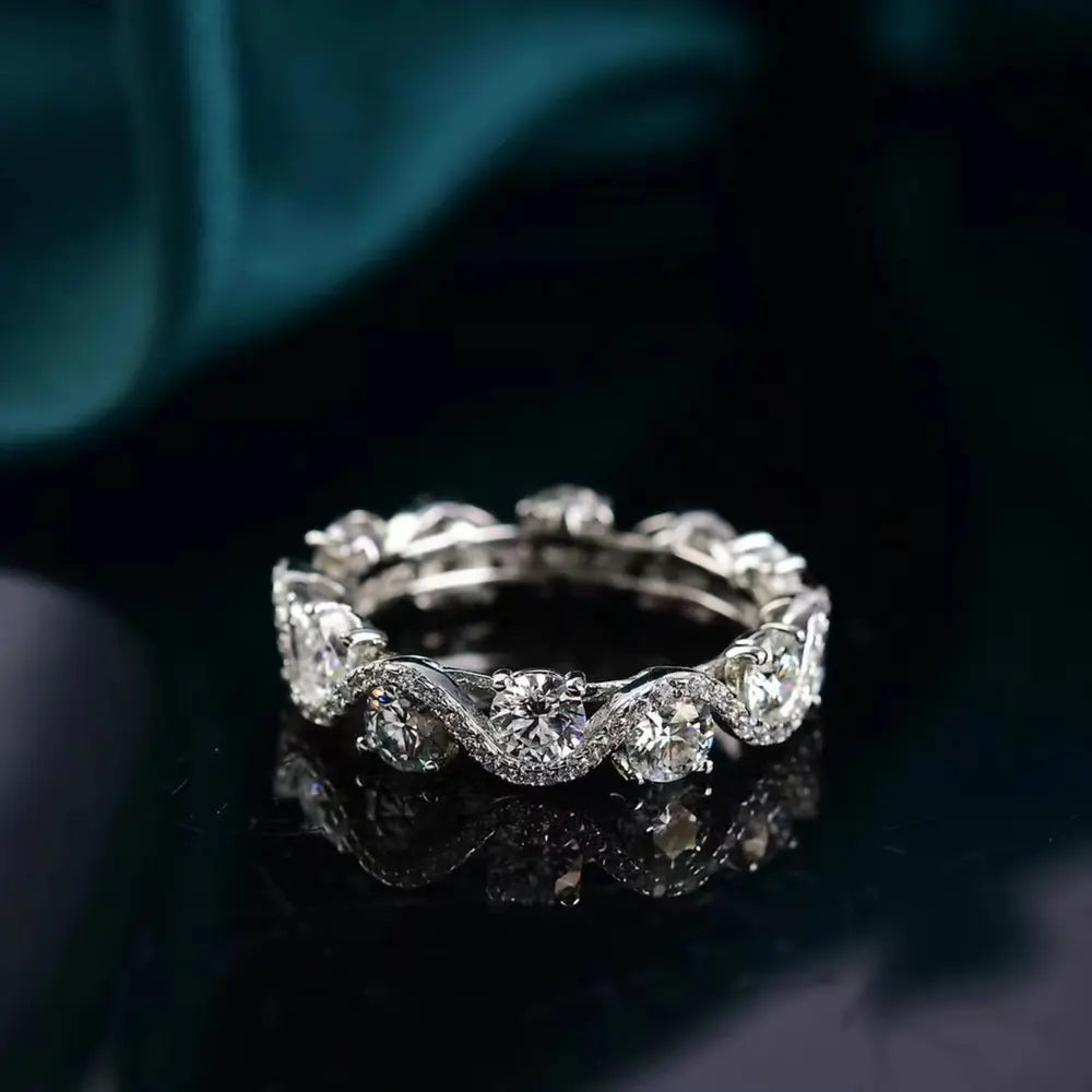 Low angled view of a floral-patterned moissanite band on dark teal fabric.