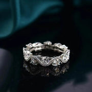 Low angled view of a floral-patterned moissanite band on dark teal fabric.