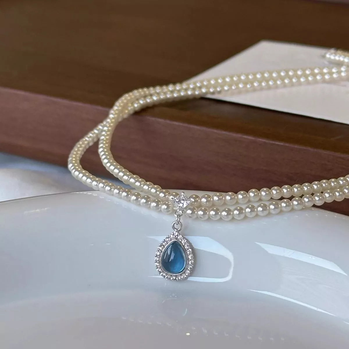 Double-layer pearl necklace and blue teardrop pendant displayed flat