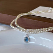 Double-layer pearl necklace and blue teardrop pendant displayed flat