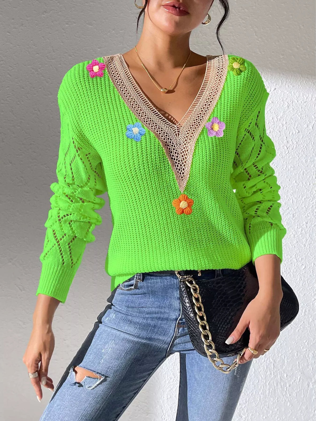 Bright green V-neck floral-appliqué sweater styled with jeans and a black bag.
