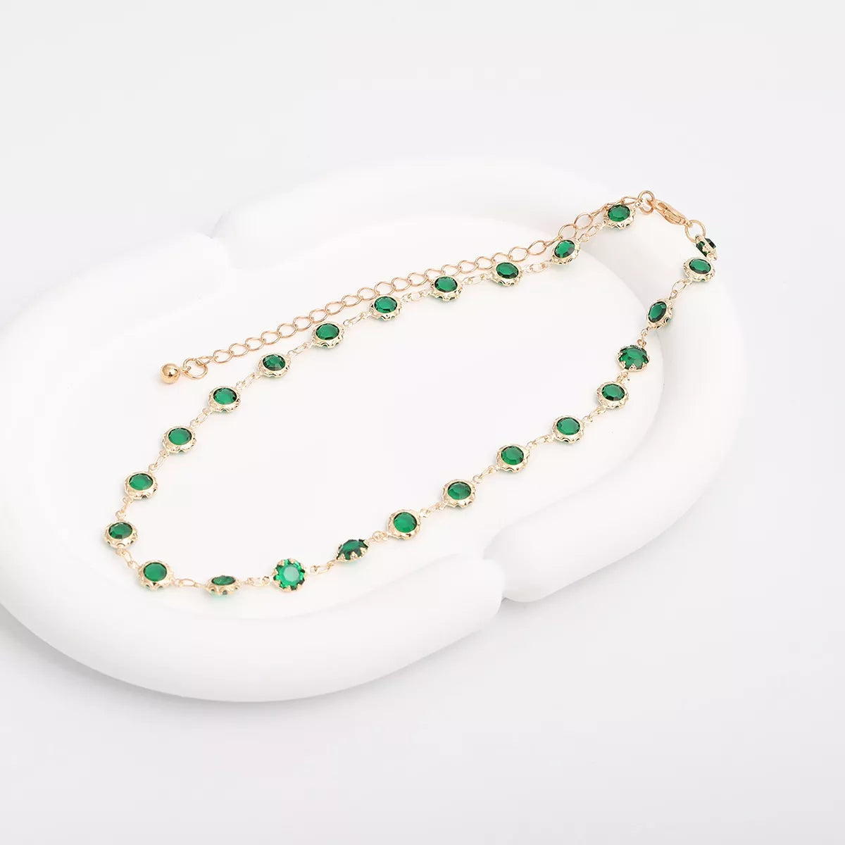 Dark green rhinestone choker with gold-tone setting, laid out on a white surface