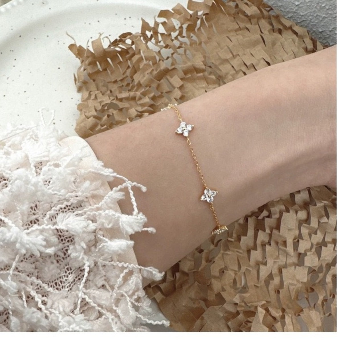 Delicate clover charm bracelet worn against a textured cream sleeve