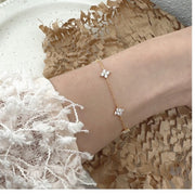 Delicate clover charm bracelet worn against a textured cream sleeve