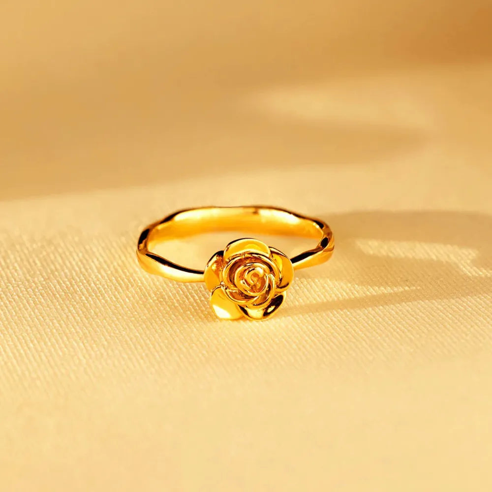 Rose-shaped gold ring displayed on a warm golden surface