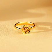 Rose-shaped gold ring displayed on a warm golden surface