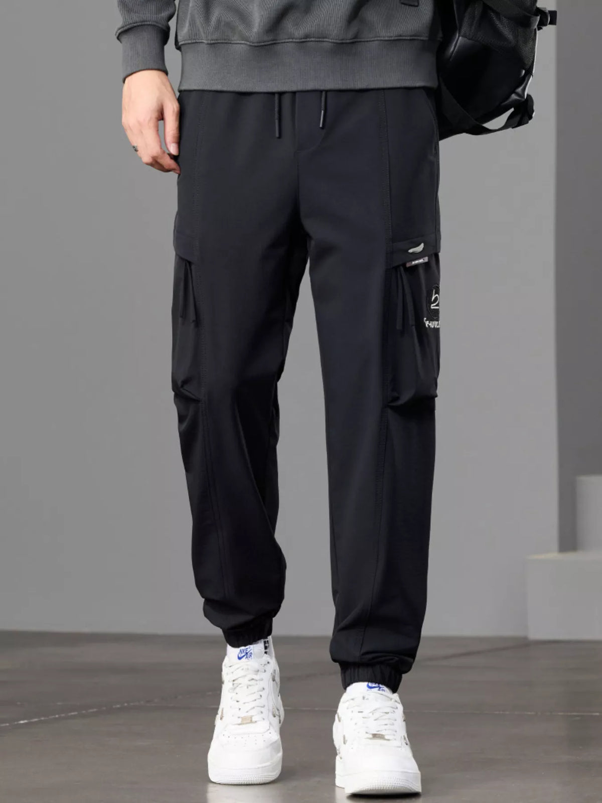 Front view of black cargo joggers styled with a gray sweatshirt and backpack.