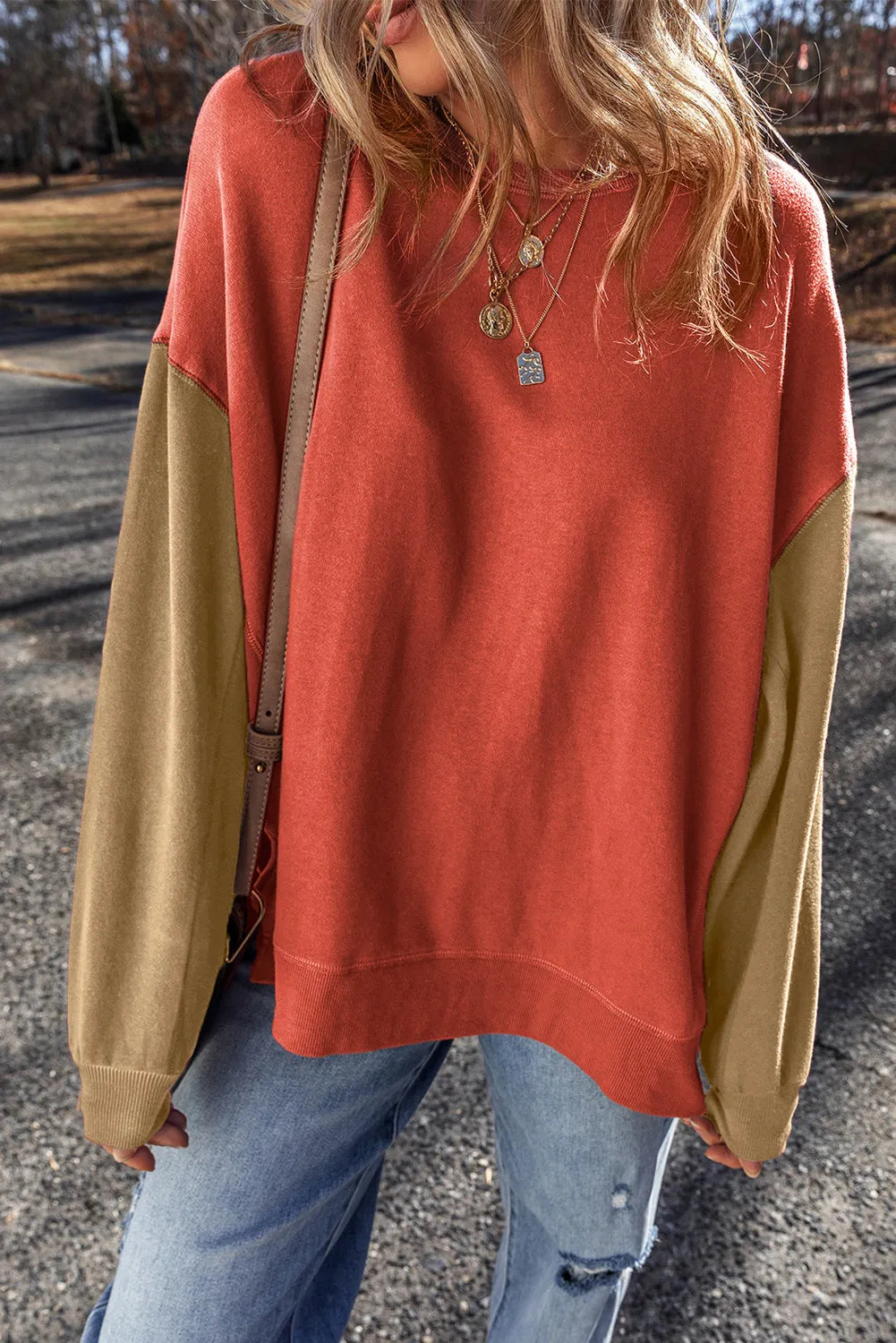 Model wearing rust sweatshirt with contrasting tan sleeves