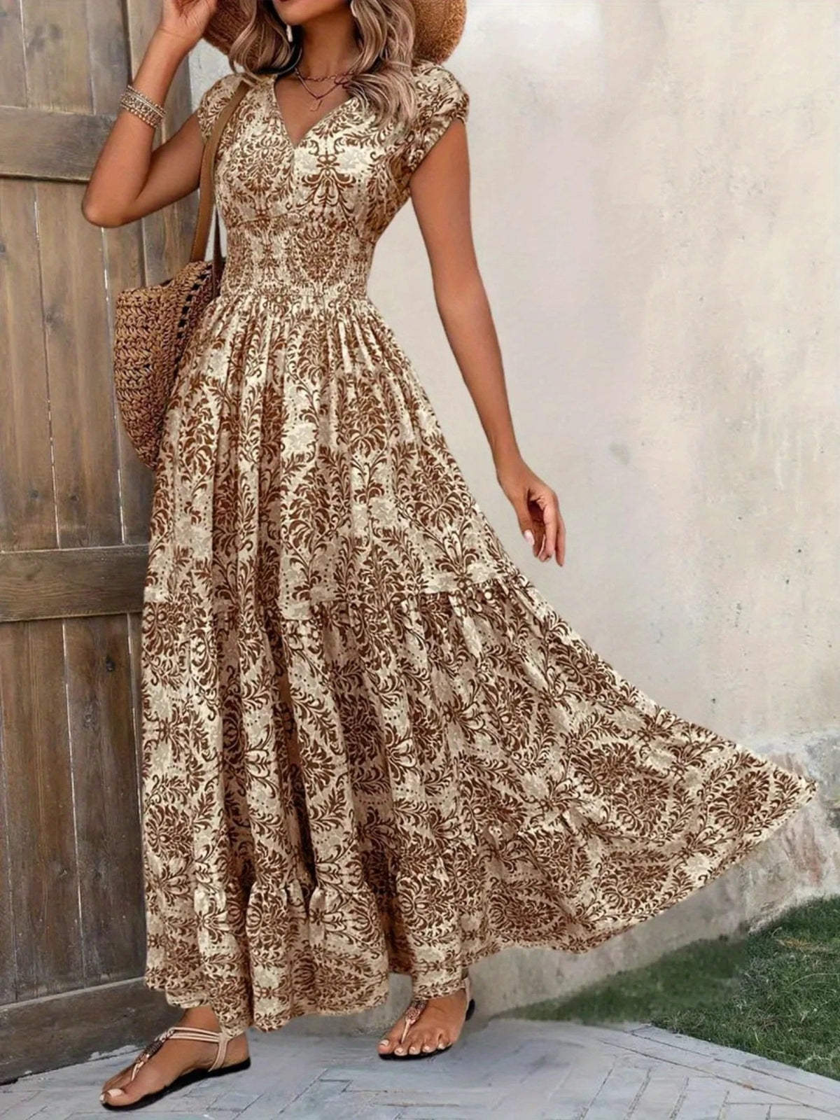 Brown floral cap-sleeve maxi dress with a V-neck and smocked waist, tiered skirt sweeping to one side.