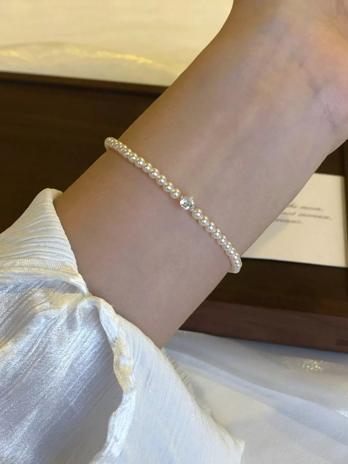 Slim adjustable pearl bracelet worn on a wrist beside a jewelry box.