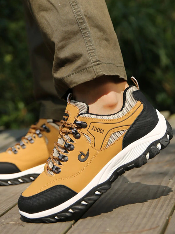 Tan lace-up shoes with black toe panels, white midsoles and chunky black outsoles, worn outdoors