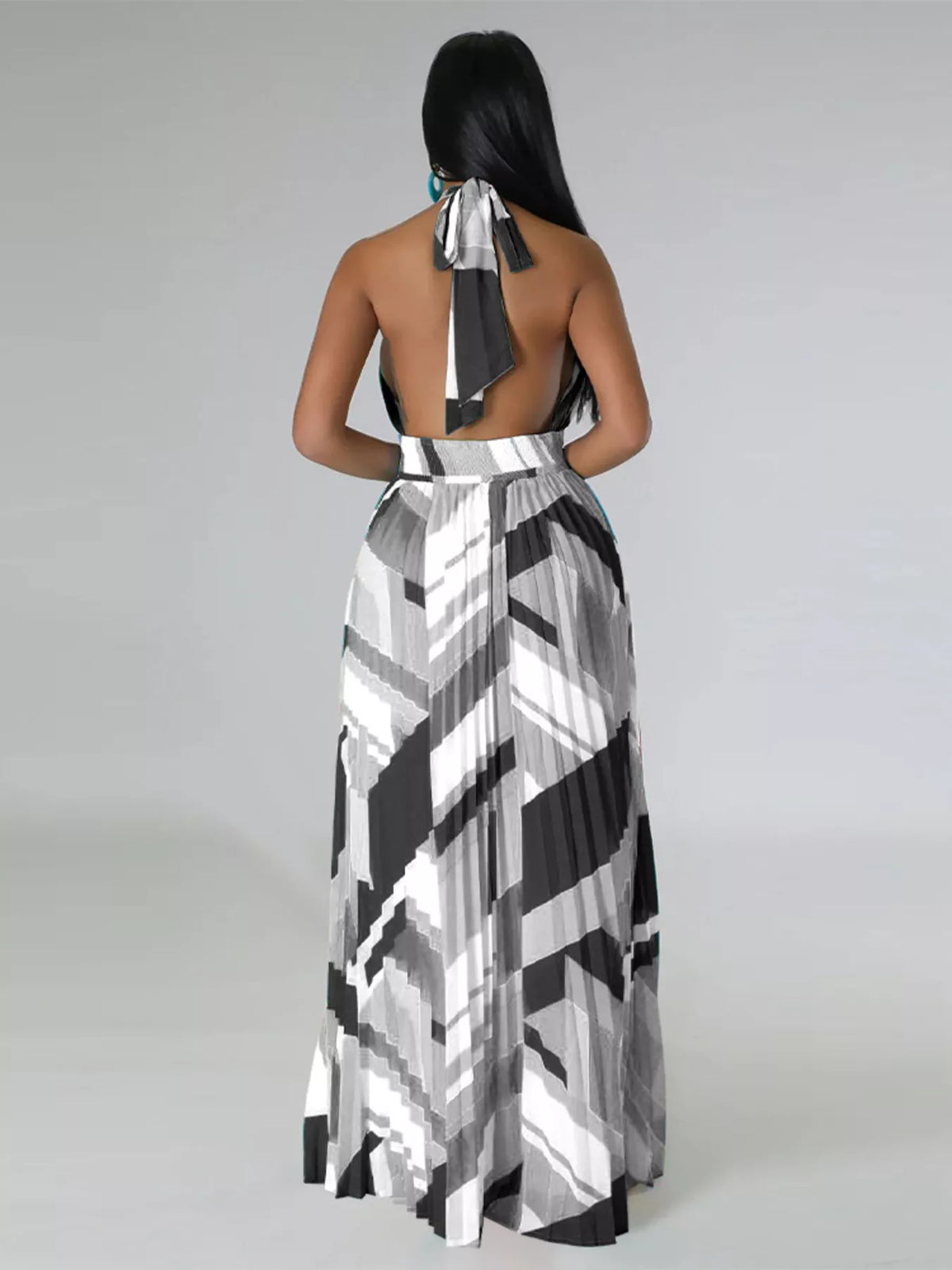 Rear view of a black-and-white geometric maxi dress showing the halter tie and long pleated skirt.