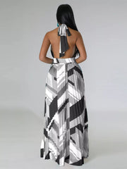 Rear view of a black-and-white geometric maxi dress showing the halter tie and long pleated skirt.