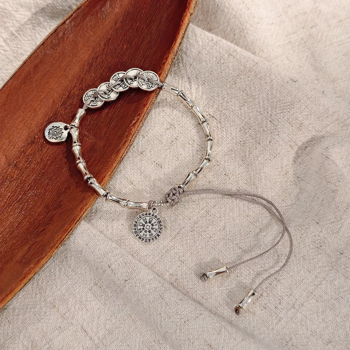 Silver-tone adjustable chain bracelet with round dangling charms on fabric beside a wooden tray.