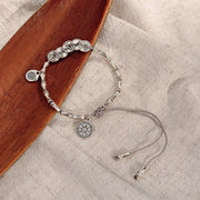Silver-tone adjustable chain bracelet with round dangling charms on fabric beside a wooden tray.