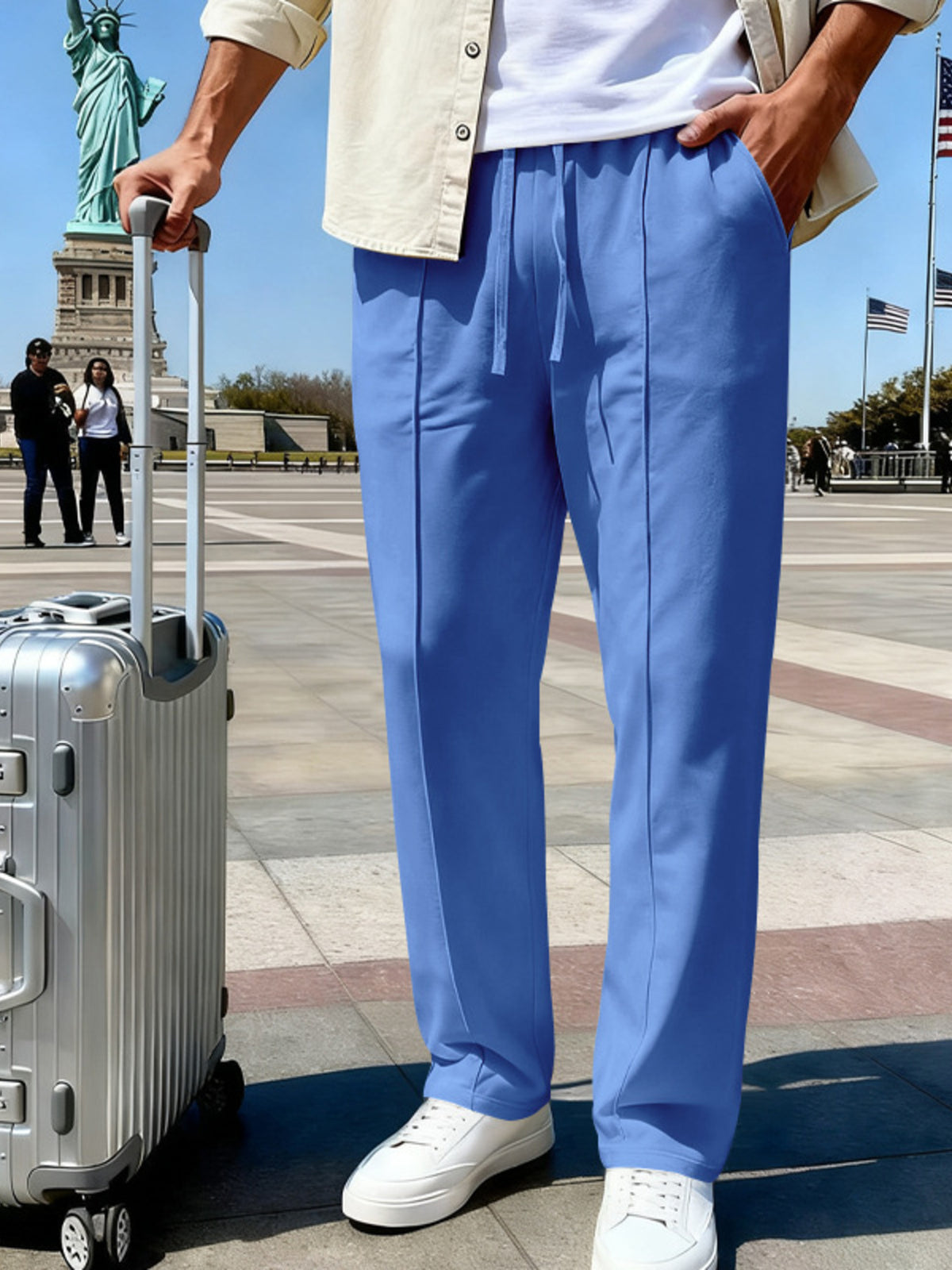 Side view of blue pants with a hand in the pocket and a rolling suitcase.