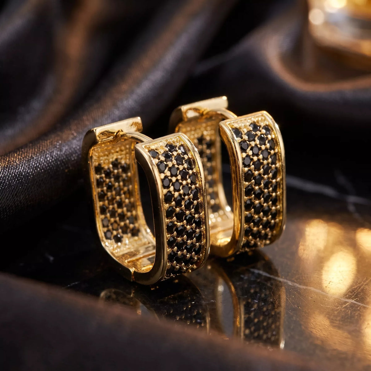 Gold-tone square hoop earrings with dark stones on black fabric