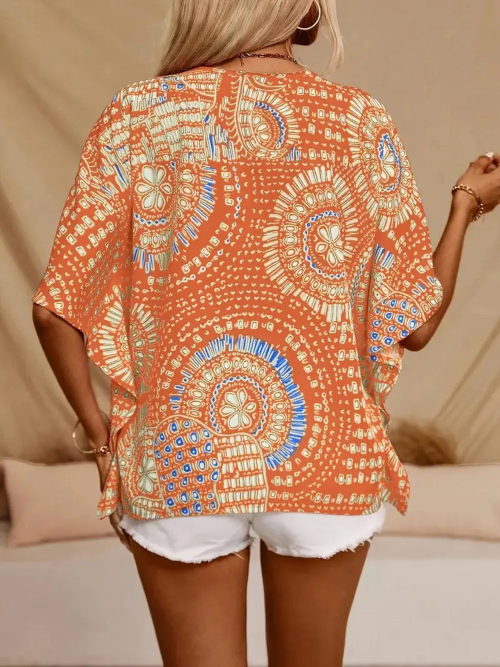 Back view of an orange and cream medallion-print blouse with loose half sleeves.