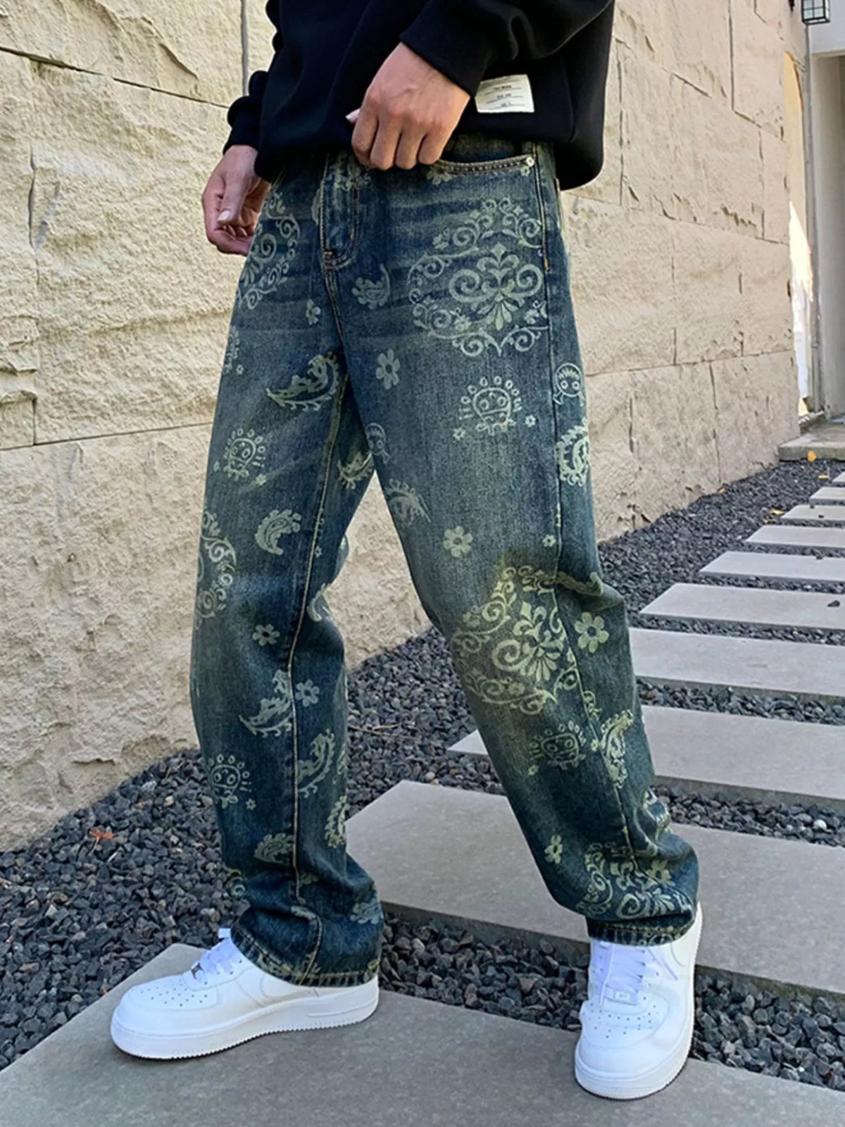 Angled front view of loose blue patterned jeans worn with white trainers