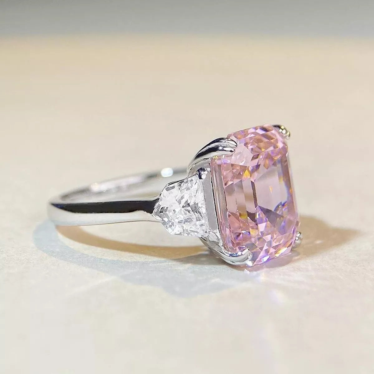 Profile view of a blush pink center stone and clear side stone on a silver-colored ring