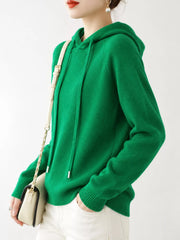 Angled view of the emerald green sweater with one hand in a white trouser pocket.