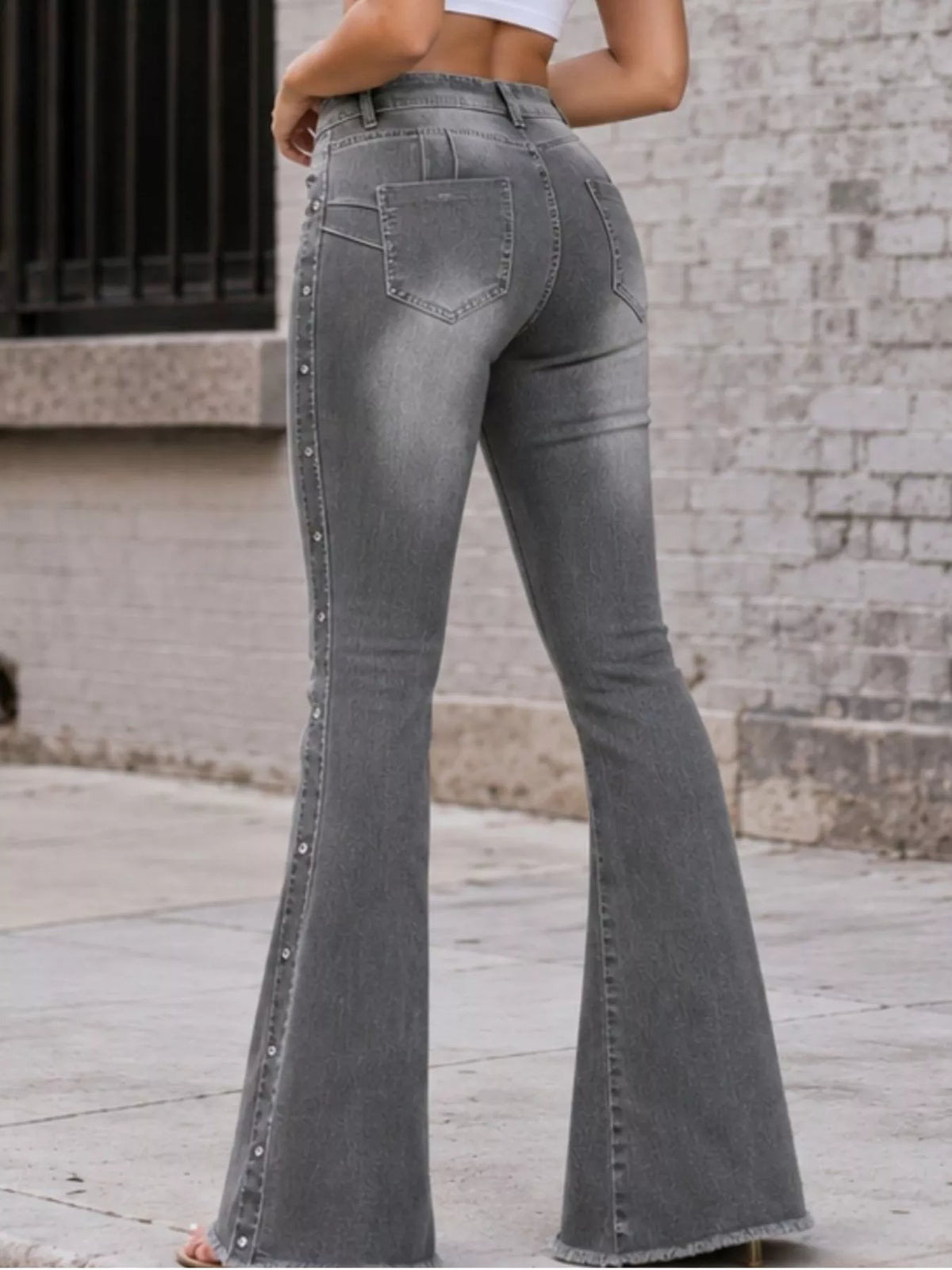 Rear view of grey flare jeans showing back pockets and studded side seams