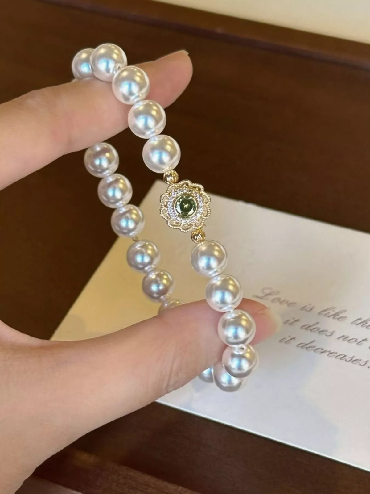 Close view of the pearl bracelet's green floral charm held between fingers
