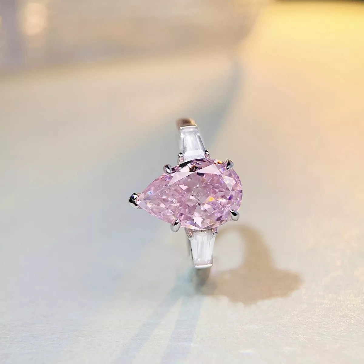 Pink pear-shaped center stone ring displayed against a turquoise ribbon.